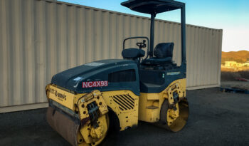 Bomag BW120AD-4 Vibratory Tandem Roller with Smooth Drum, featuring a compact design and an open canopy, parked on a dirt lot in front of a beige shipping container at sunset.